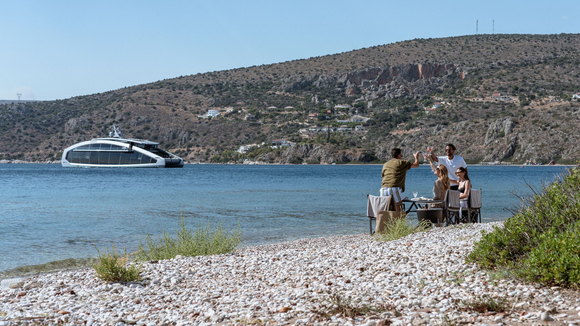 a group of friends having bbq on a greek beach with the iyc yacht this is it in the background