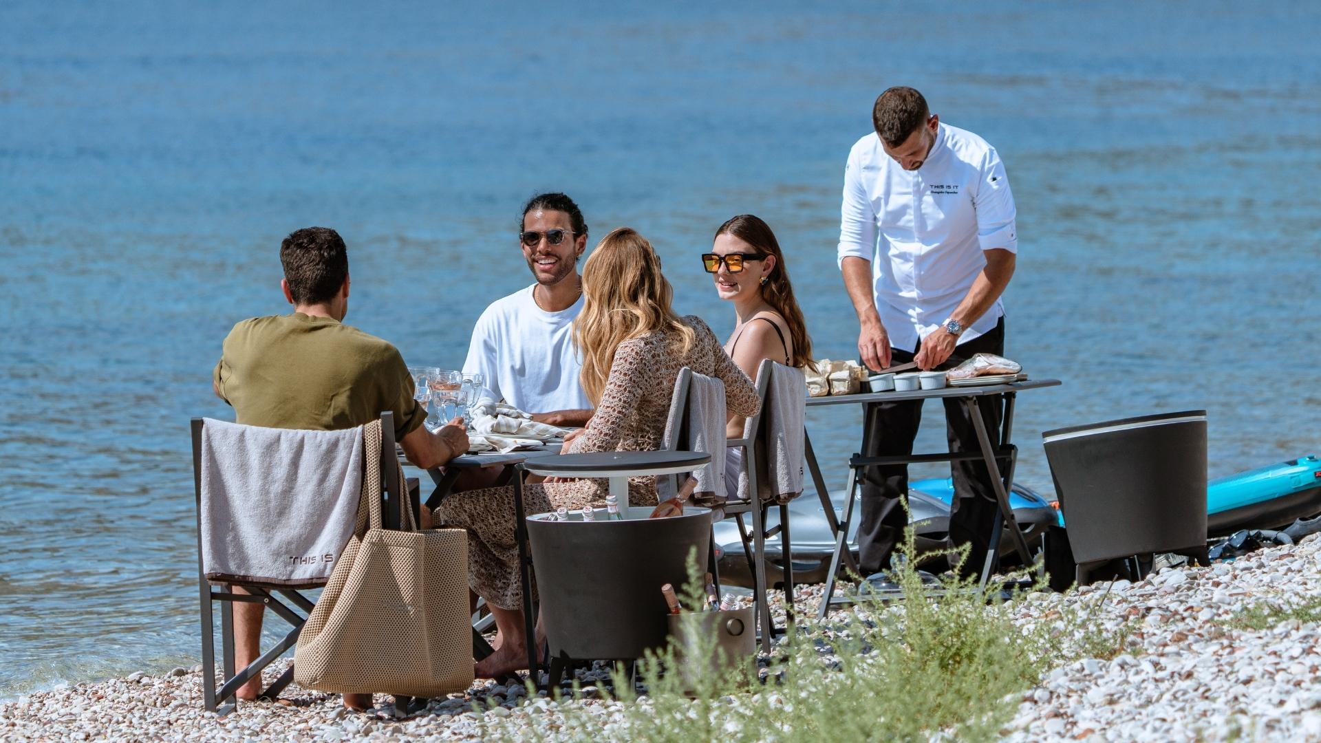 a party of 4 people dining on a beach private setup while a yacht chef prepares food