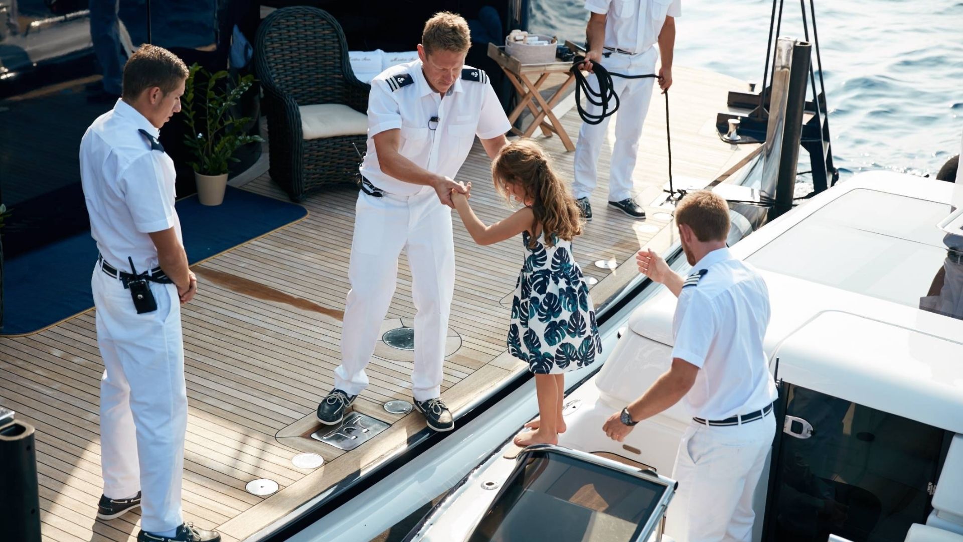 a crew member of iyc yacht assists a young girl step onboard