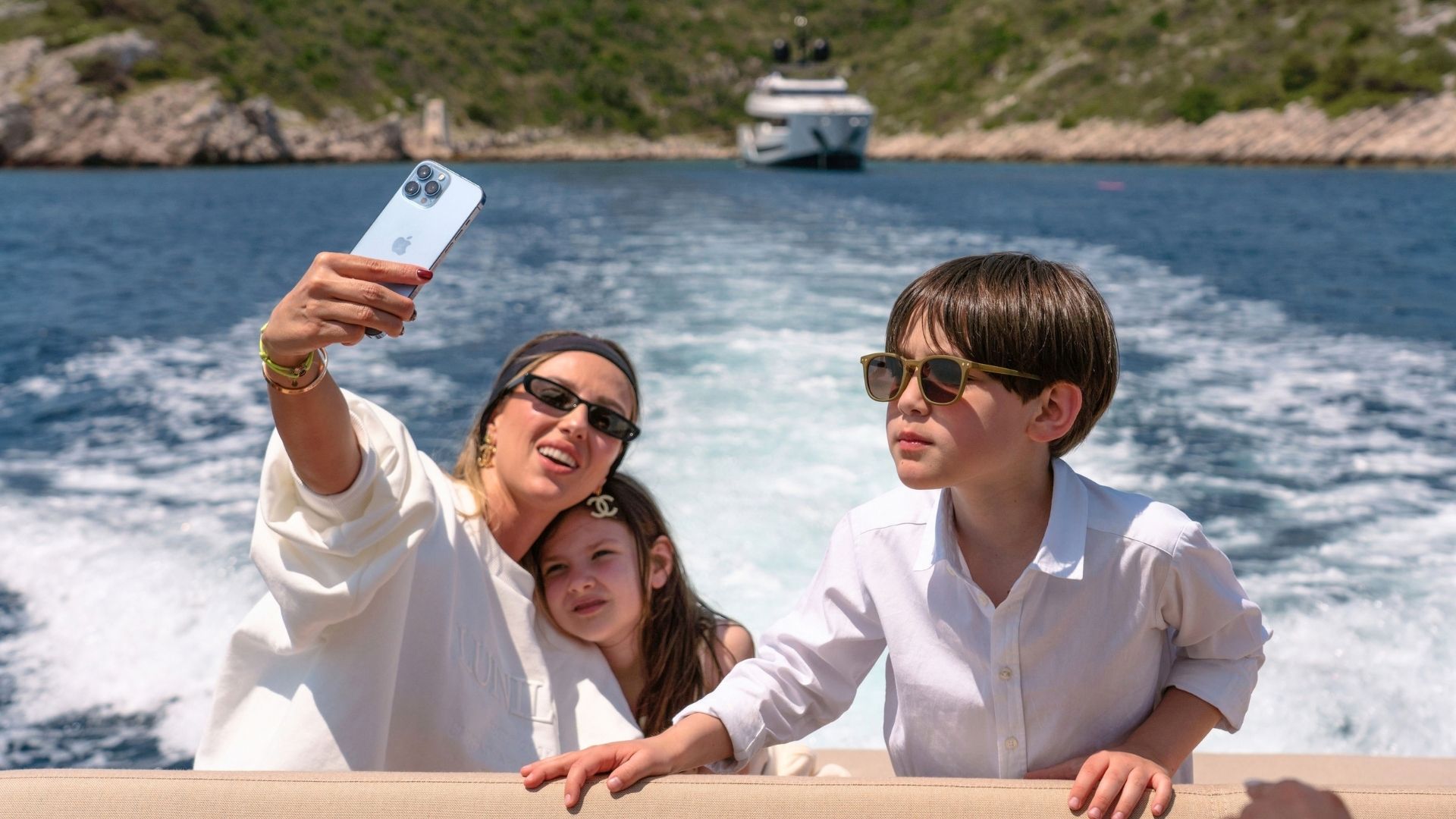 a family of three taking a selfie with an iyc yacht on the background