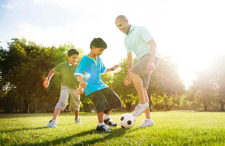 Two young boys and an adult playing soccer outdoors