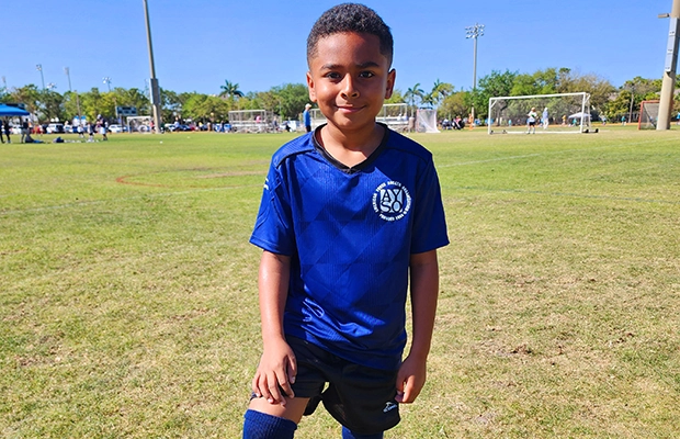 A boy posing for the camera on a soccer field while wearing a blue uniform.