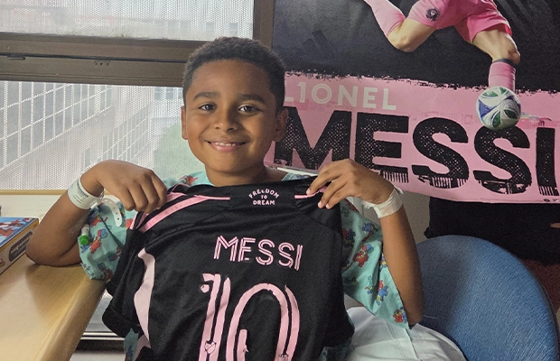Children smiling at the camera while showing off a Lionel Messi jersey.