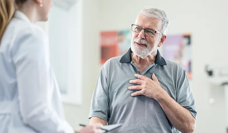 An older man touching his chest, he is speaking to a medical professional