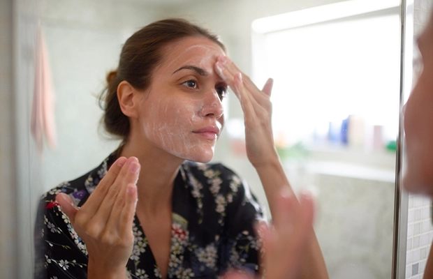 woman applying cream on her face in front of the mirror