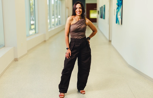 Woman wearing black trousers and a brown blouse, posing and smiling at the camera.