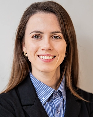 Close-up of a woman smiling at the camera with a beige background behind her.
