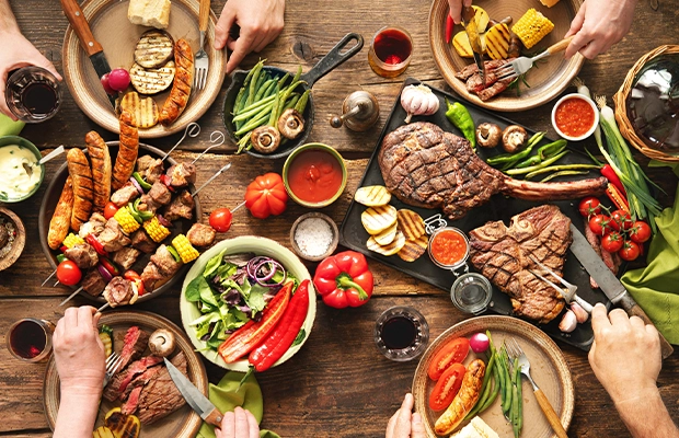 Table full of dishes with protein, meat, sausages, chicken, and some vegetables like paprika, corn, tomatoes and sauces