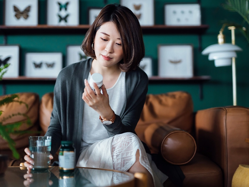 Woman reading a medicine bottle, while holding a glass of water in her hand