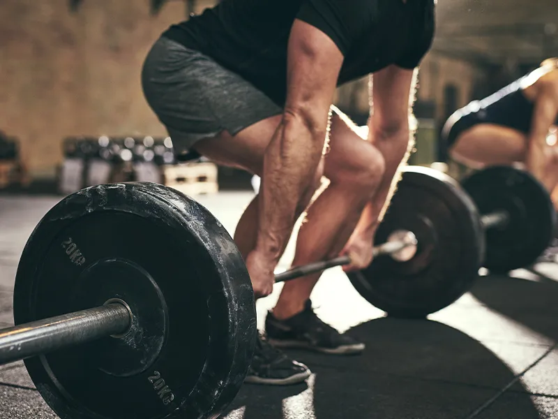 man in gray shorts and black t-shirt lifting weights in the gym