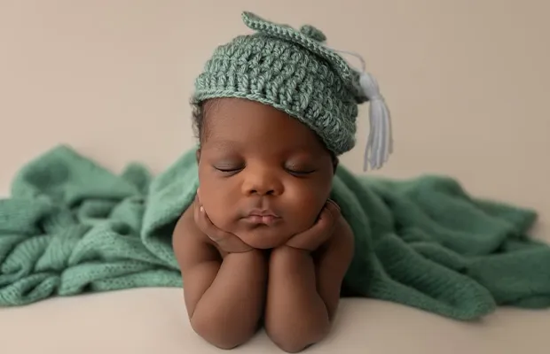 Professional photograph of a small baby with his eyes closed wearing a green wool hat