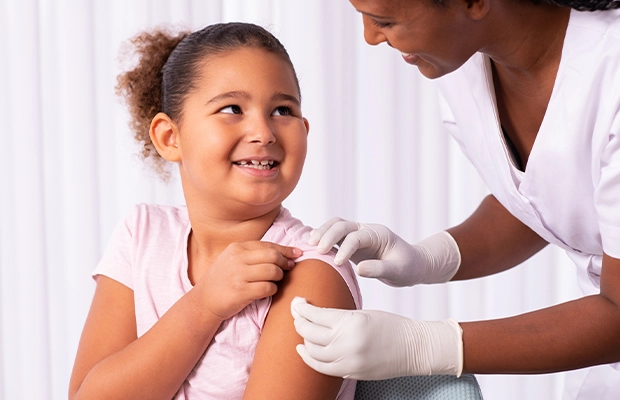 A girl smiling at her doctor while she places a cotton ball on her arm.