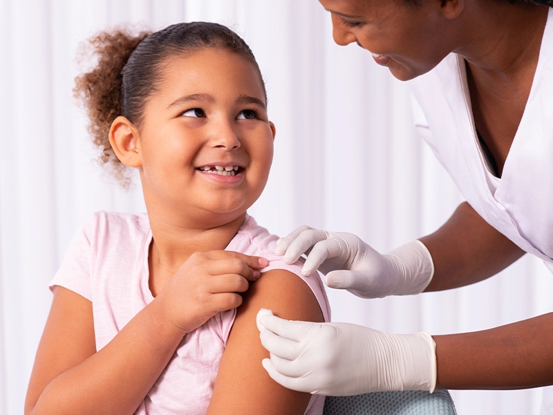 A girl smiling at her doctor while she places a cotton ball on her arm.