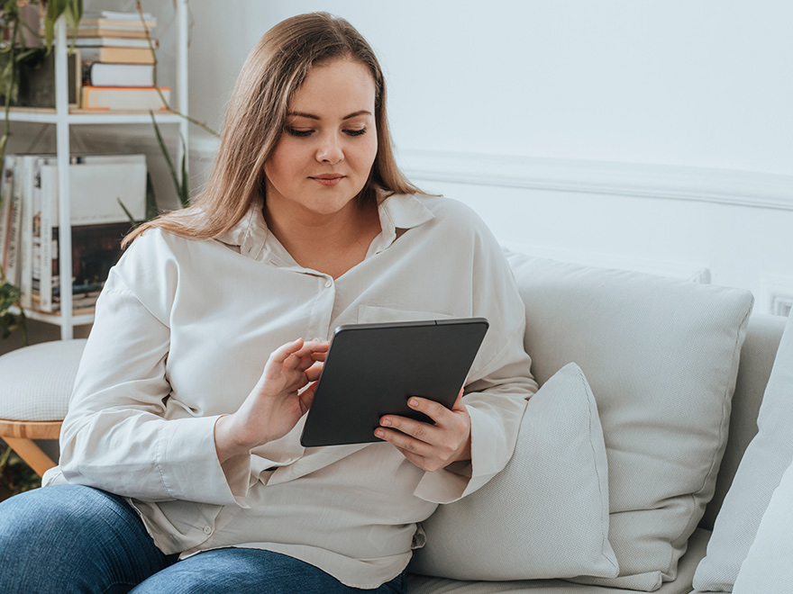 Woman using her tablet as she is seated on her couch