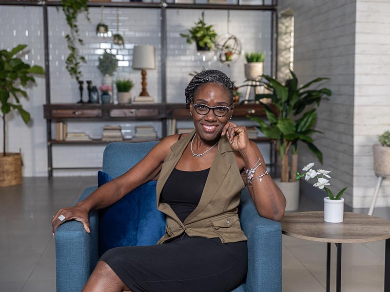 Robin sitting in a chair and smiling at the camera, she is wearing a black dress
