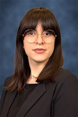 Close-up of a smiling woman dressed elegantly, with a blue background behind her.