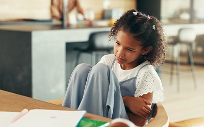 Little girl sitting in a school classroom with her legs drawn up towards her