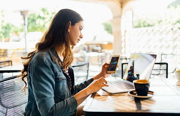 A woman sitting outdoors, she is sitting and looking at her phone and laptop