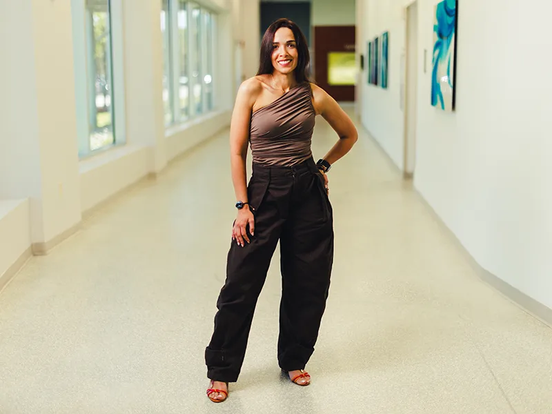 Woman wearing black trousers and a brown blouse, posing and smiling at the camera.