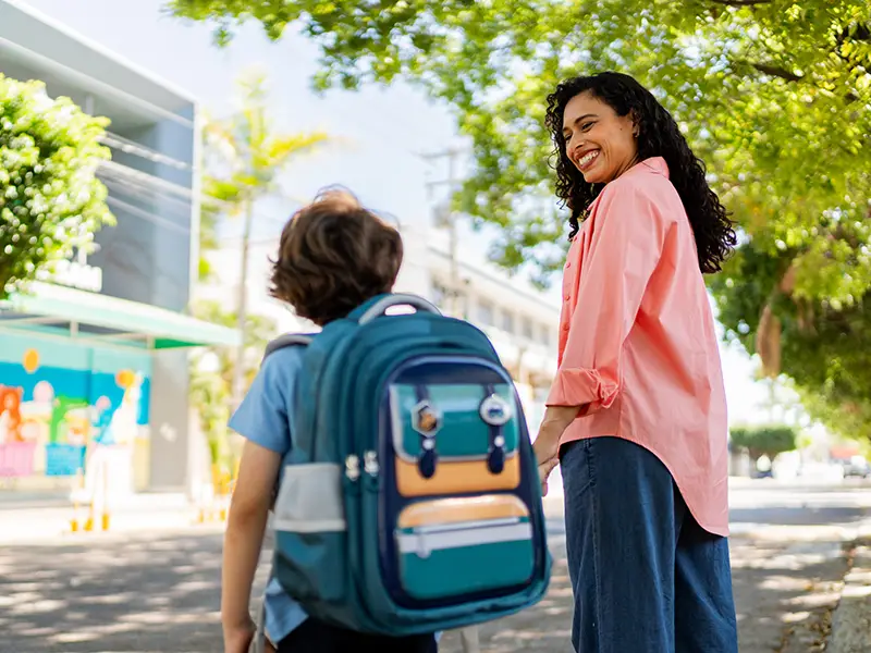 A mom and young boy walking, he has a backpack on