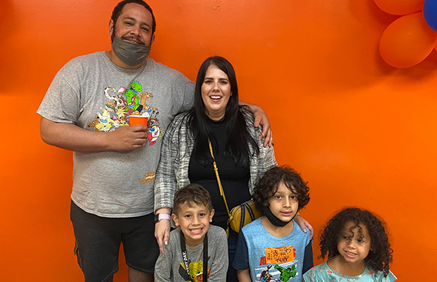 A man and woman standing behind three young children, they all smile at the camera