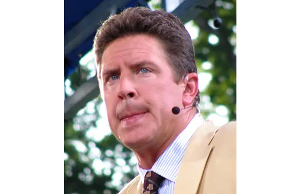 A man with a small microphone looking out, he is wearing a suit and tie