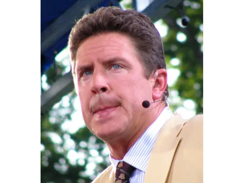 A man with a small microphone looking out, he is wearing a suit and tie