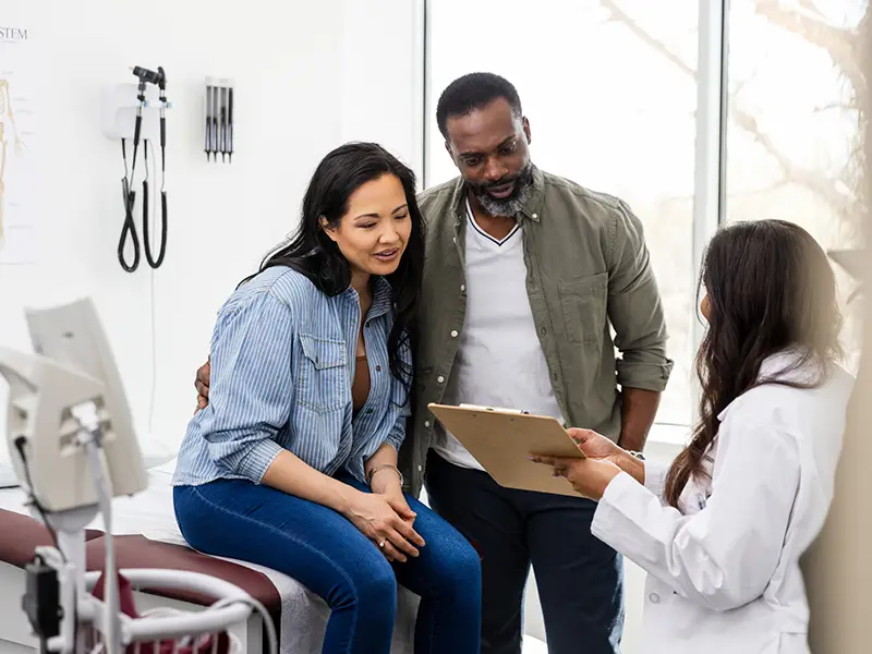 A man and woman sitting together at a doctors office looking over a document a doctor is sharing with them