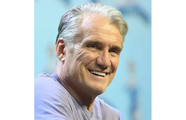 A middle-aged man looking out, he has on a purple top and smiles