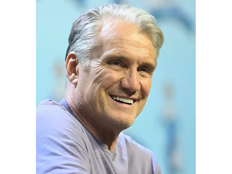A middle-aged man looking out, he has on a purple top and smiles