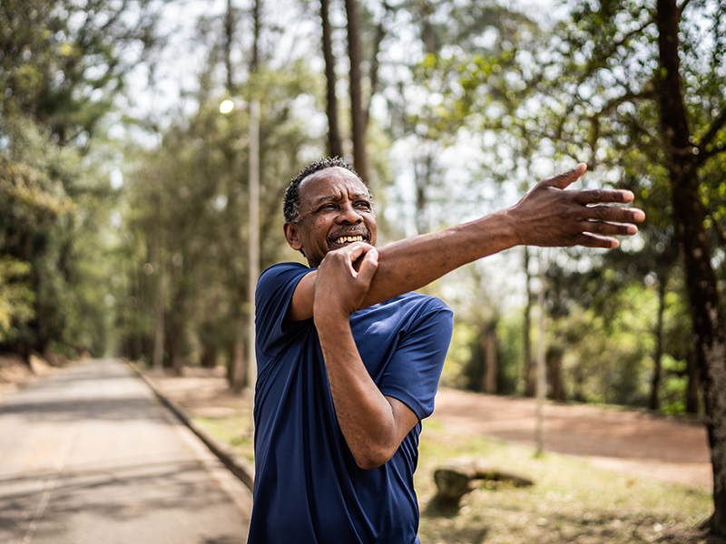 An older male outdoors, he is stretching his right arm