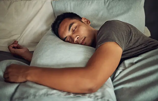 A man sleeping in bed, he has his left hand over his pillow