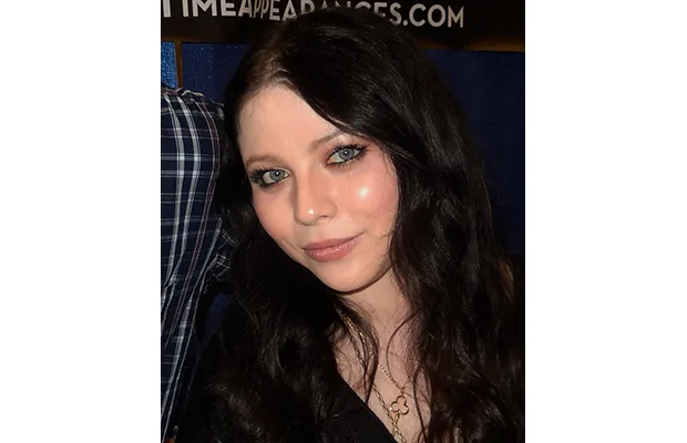A closeup of a woman, she has long dark hair and is looking at the camera