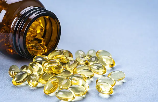 A closeup of a pill bottle tipped over with yellow tinted vitamins scattered on the floor