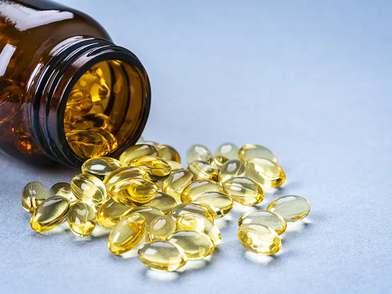 A closeup of a pill bottle tipped over with yellow tinted vitamins scattered on the floor