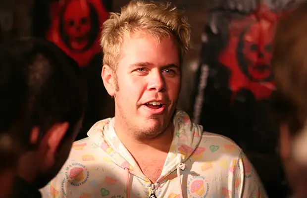 A closeup of a man speaking, he has short blonde hair and is wearing a sweatshirt