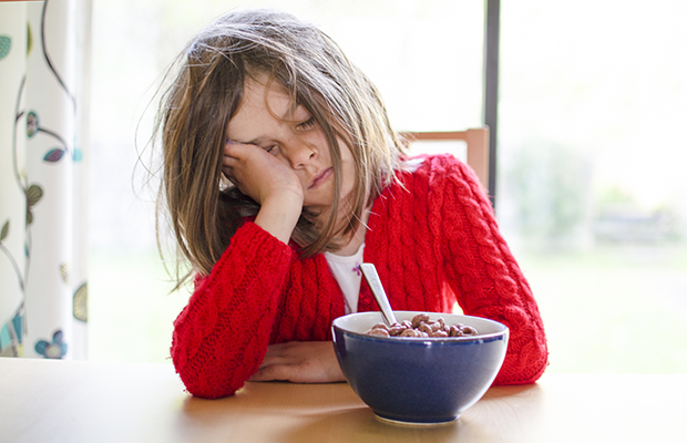 A child falling asleep in front of their cereal bowl as they sit at the dining room table