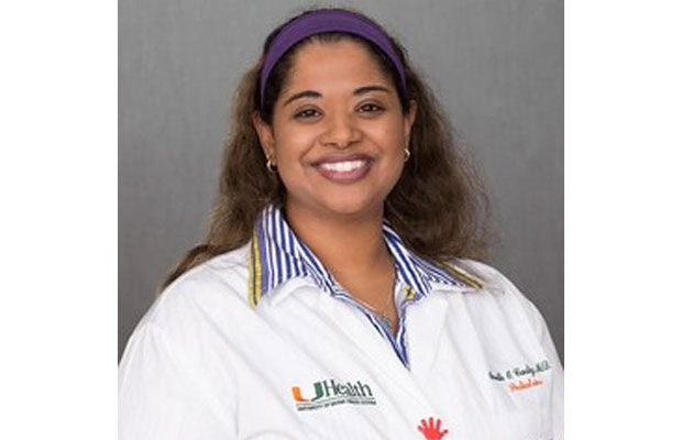 A closeup of a physician, she is smiling at the camera, she has on a white coat and purple headband