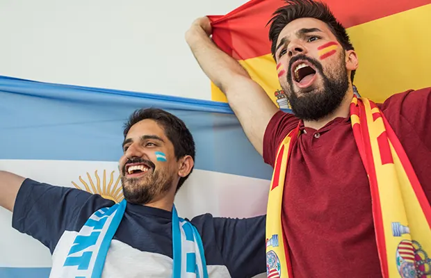 Two people cheering, one is wearing Spain colors, another Argentina colors