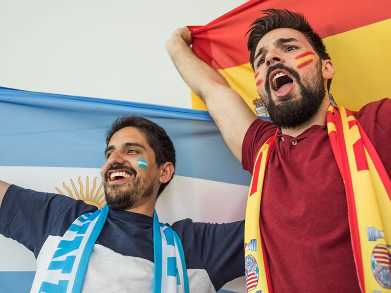 Two people cheering, one is wearing Spain colors, another Argentina colors
