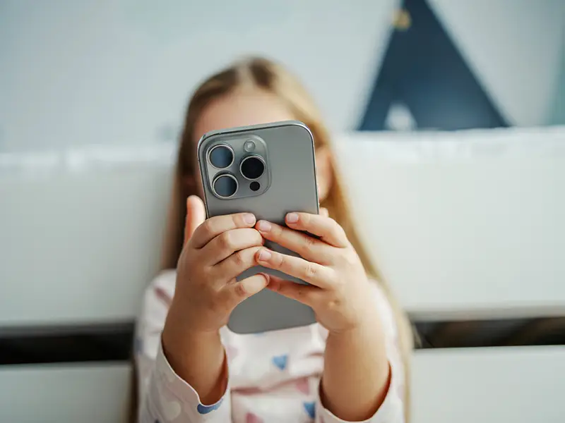 A young girl holding a mobile phone, the mobile phone covers her face
