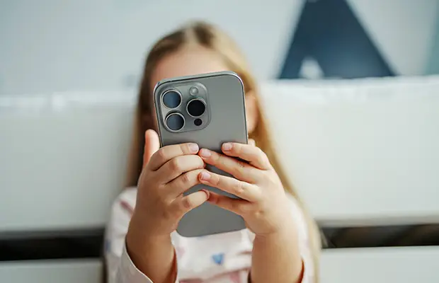 A young girl holding a mobile phone, the mobile phone covers her face