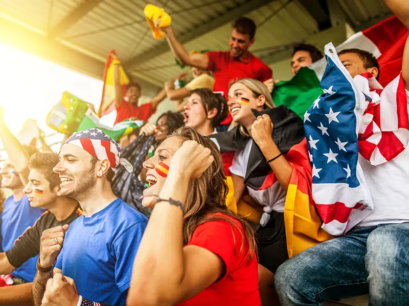 A crowd of people sitting at a sporting event and rooting for their team, they have USA colors and attire on