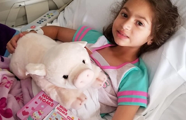 little girl lying on hospital stretcher with many stuffed animals around