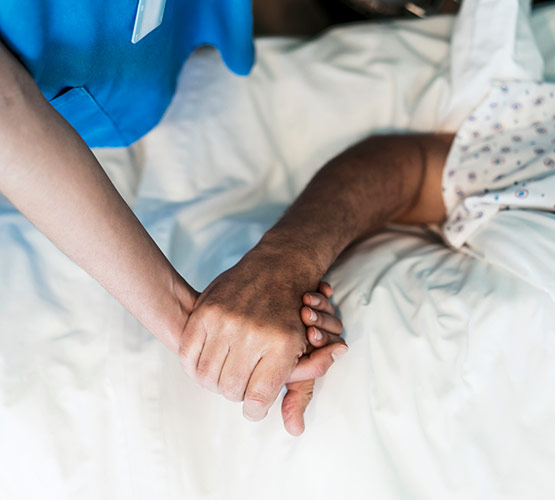 Zoomed image of a nurse holding a patient's hand as they lay on a hospital bed