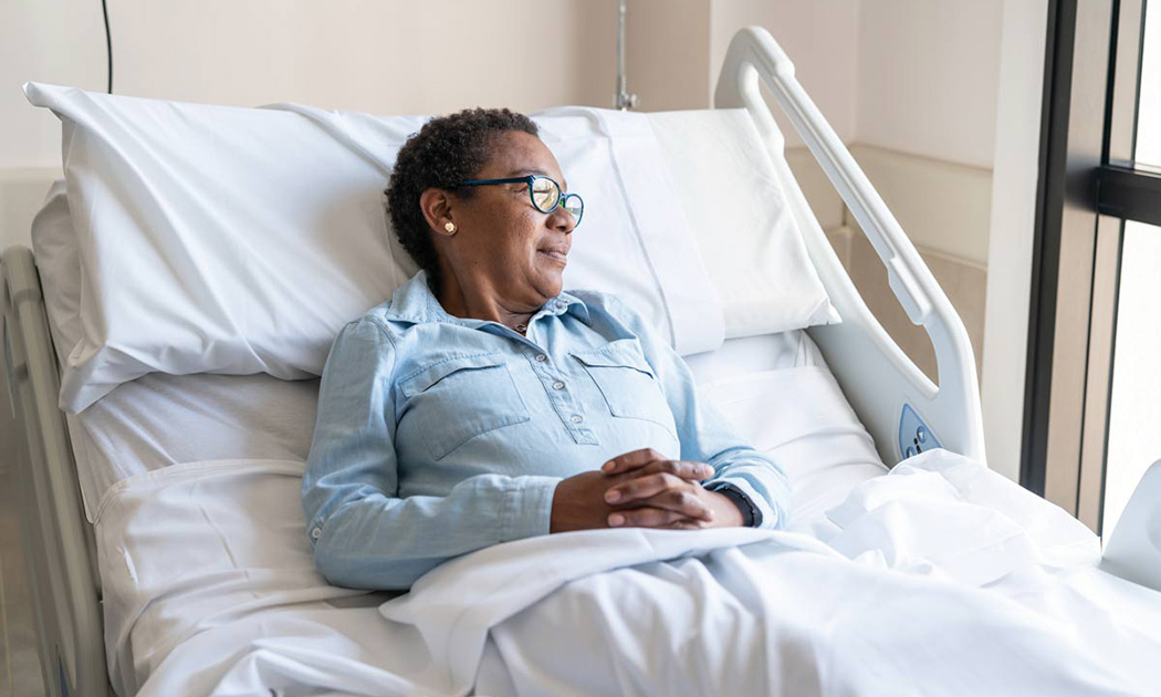 An older woman laying in a hospital bed smiling as she looks out the window