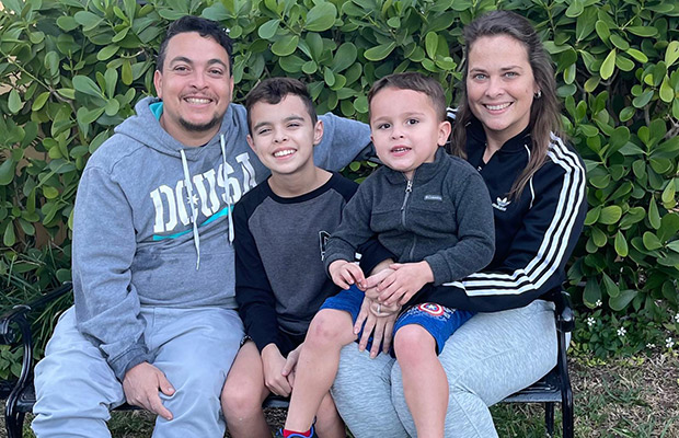A family of four sitting and smiling, there is a women, a men, and two young boys