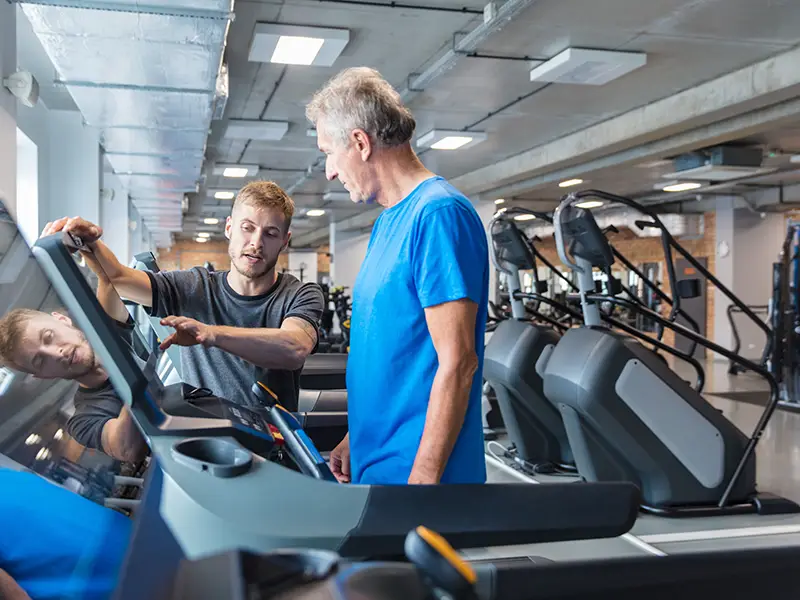 Trainer helping an elderly man use a treadmill