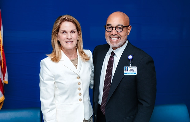 A man and a woman in formal wear smiling at the camera next to the United States flag.