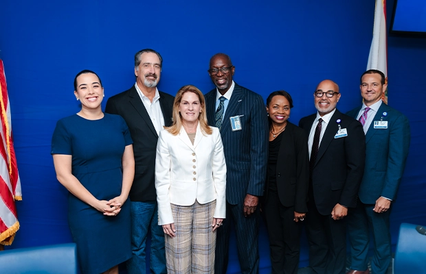 A group of people dressed in formal attire posing and smiling for the camera next to the United States flag.